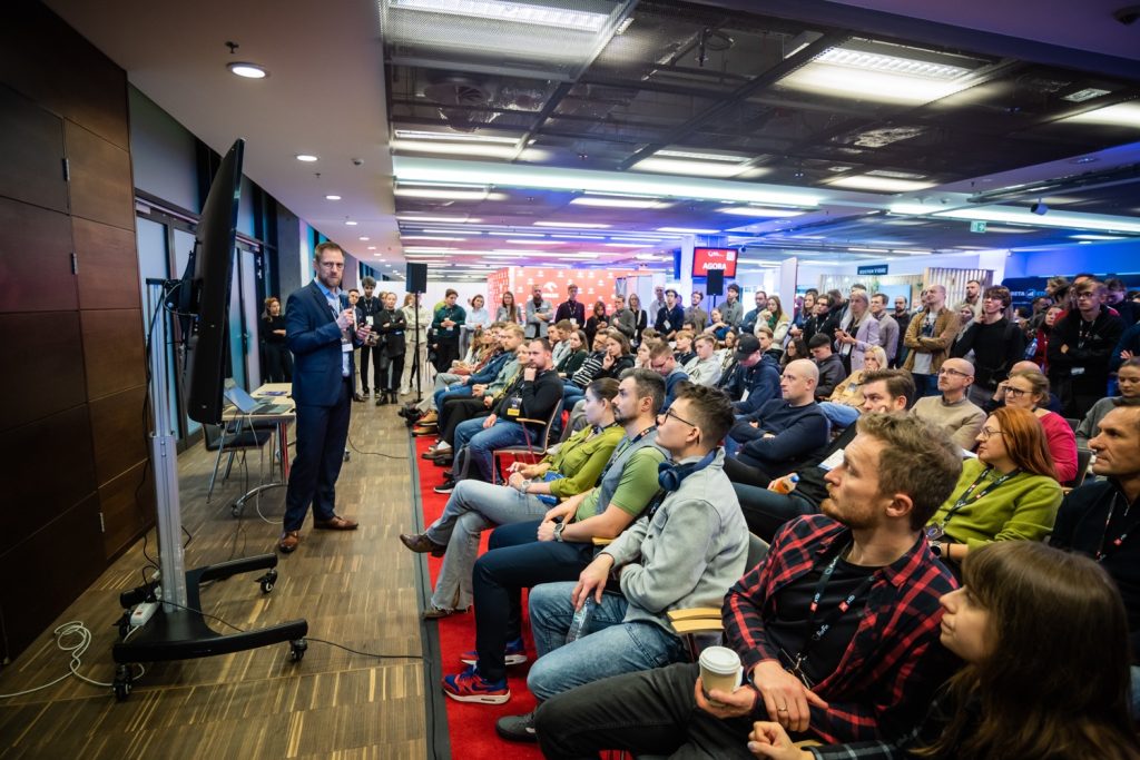 ForFin 2025 - prelegent wygłasza wykład do tłumu uczestników konferencji finansowej sieddzących na czerwonych fotelach, niebieskie oświetlenie, sala konferencyjna, edukacja inwestorów